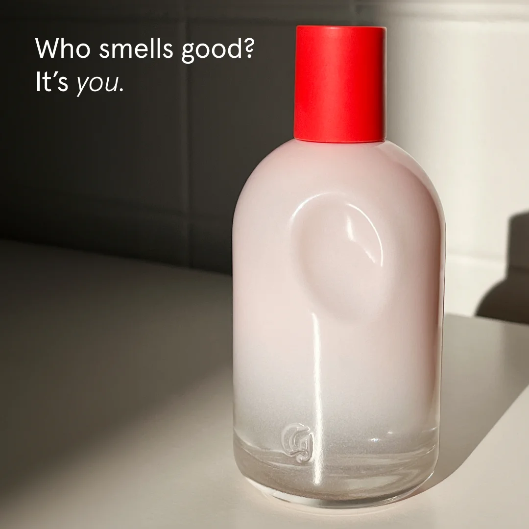 Glossier You perfume bottle with red cap against dark tile background with white headline Who smells good? It's you.