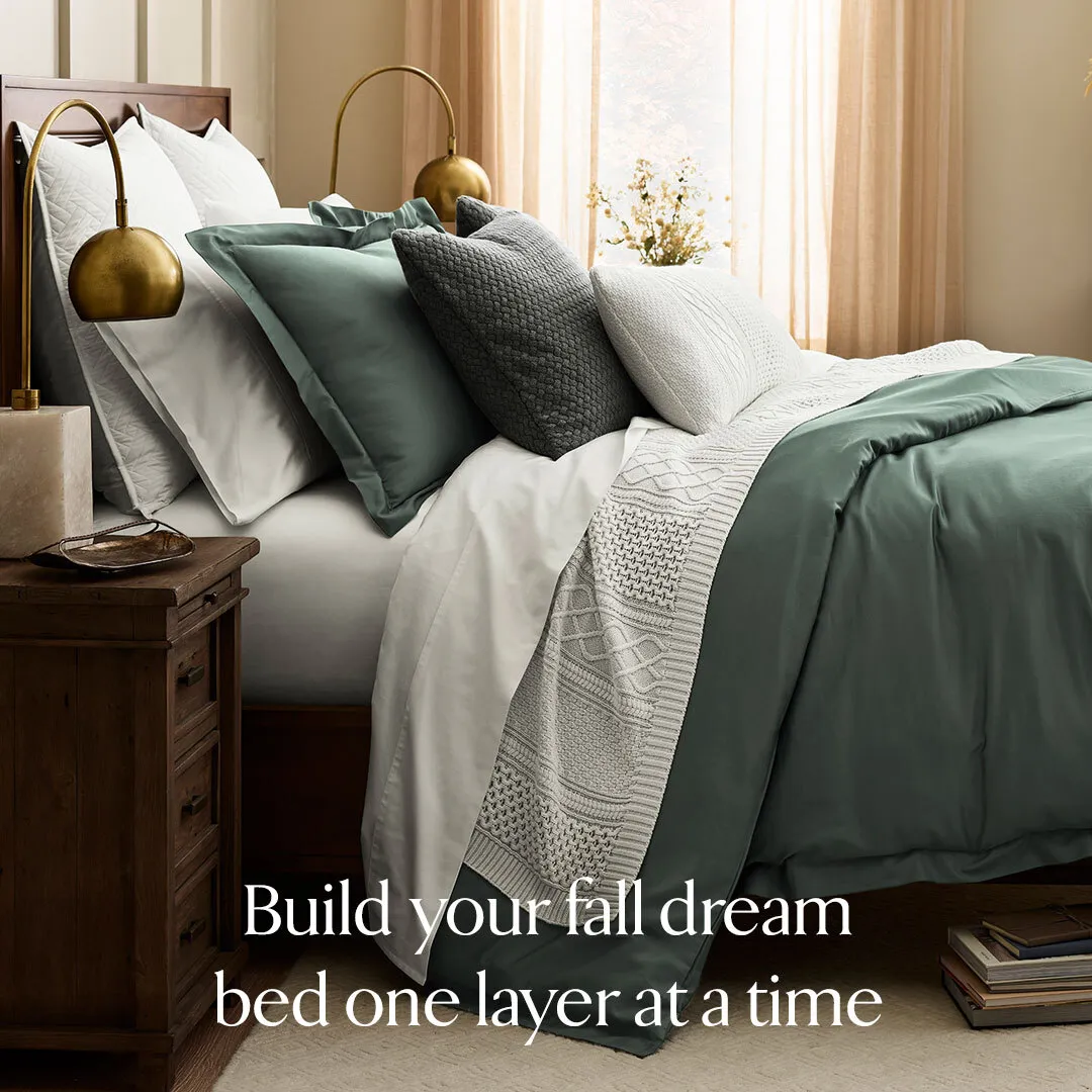 Boll & Branch luxury ad example: a made bed in sage and white with brass lamps and one serif headline