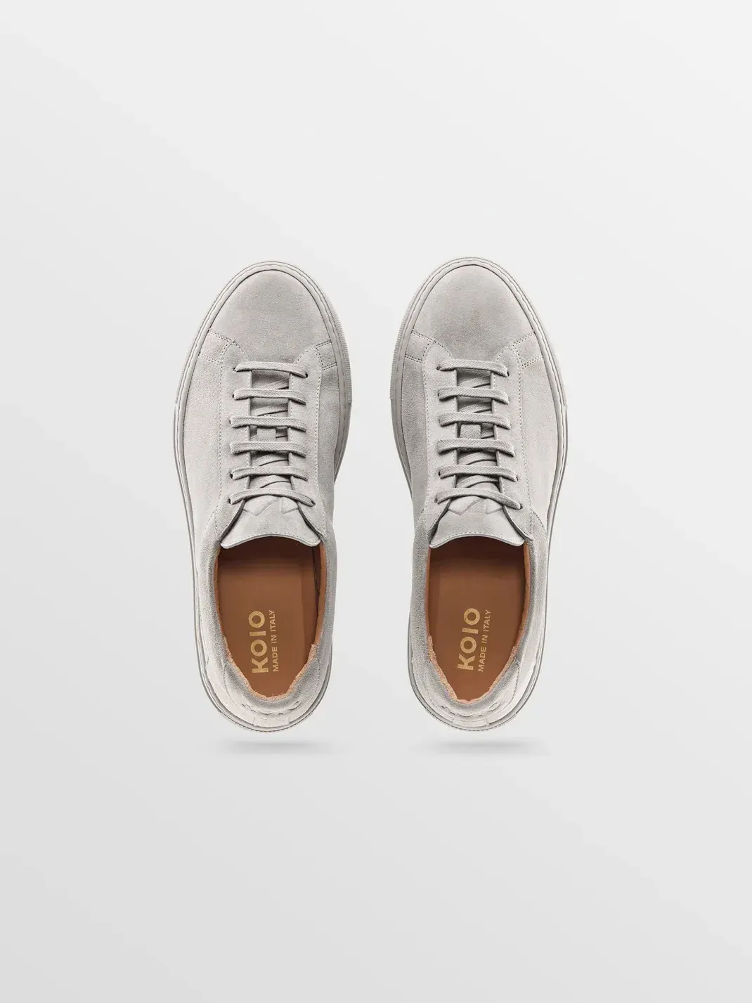 Koio sneaker ad example: a pair of gray suede sneakers shot from directly above on a pale gradient, tan insoles visible