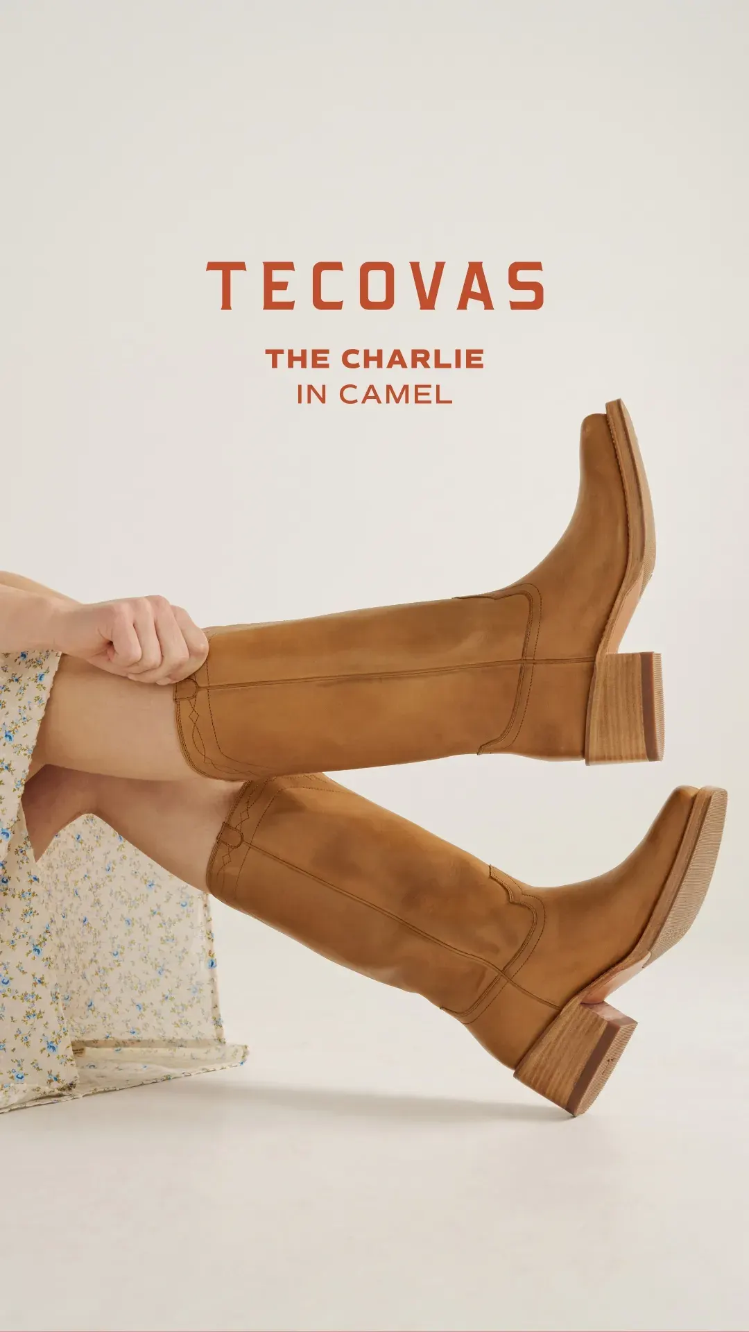Tecovas boot ad example: two legs in camel suede knee-high boots crossed against a pale backdrop, The Charlie in camel