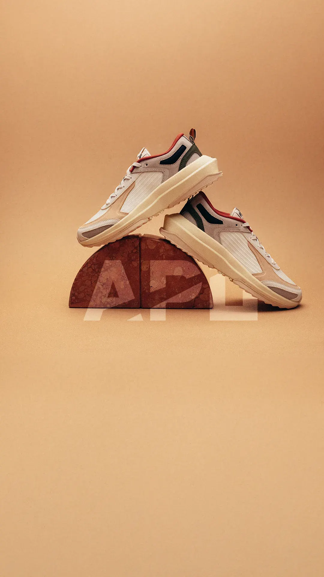 APL sneaker ad example: a pair of sneakers balanced on a half-round APL letterform block on a peach backdrop