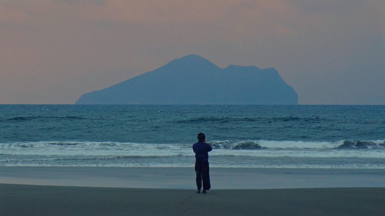 Anthropic World Cup film There is hope in hard questions: a person standing on a beach facing an island at dusk
